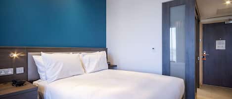 A modern hotel room with a large bed, a wooden nightstand, and a blue accent wall.