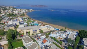 Vista aérea de un complejo turístico frente al mar, con playa, piscina y varios edificios.