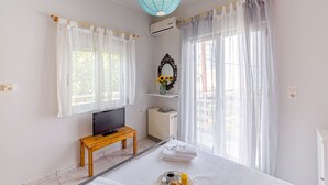 Habitación de hotel con cama, televisor sobre una mesa de madera, aire acondicionado y vistas al exterior a través de cortinas translúcidas.