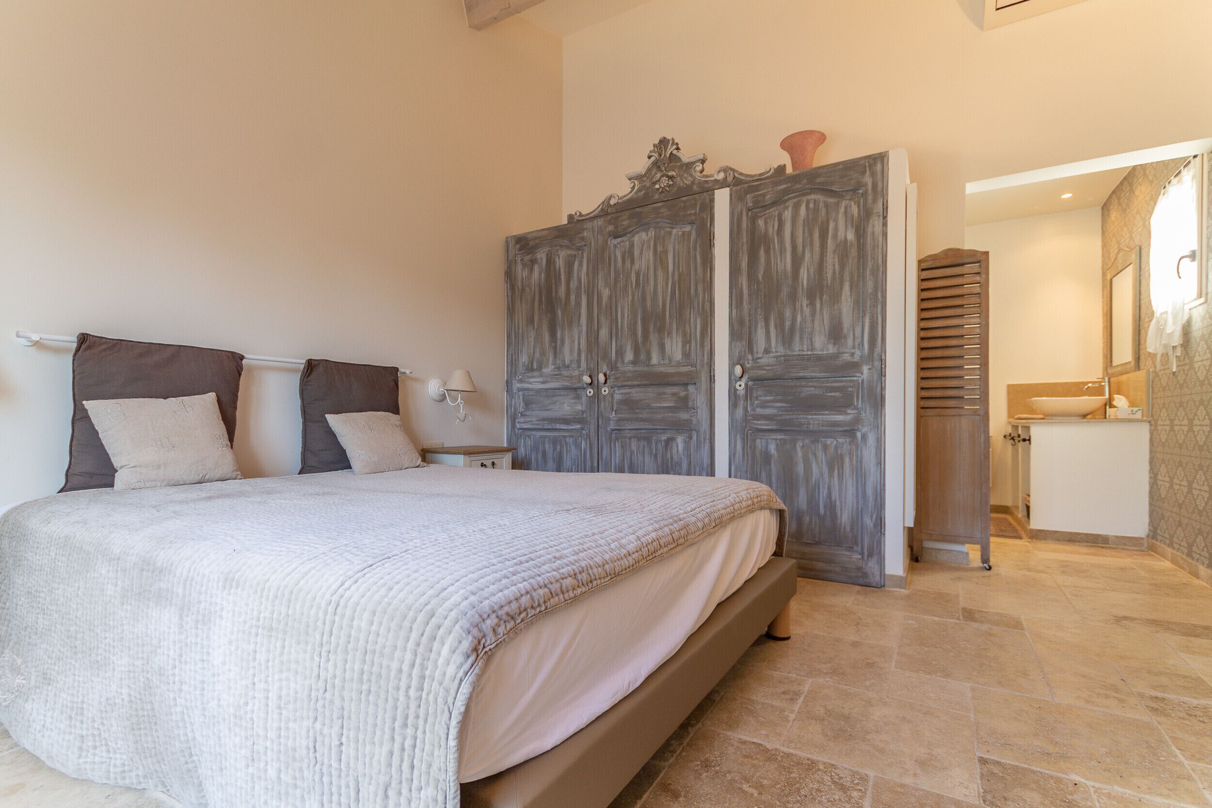 Une chambre à coucher comprenant un lit, une armoire, une table de chevet, et une salle de bain visible à travers une porte ouverte.