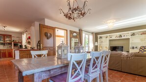 A spacious kitchen with a wooden table and white chairs, a chandelier, and a TV in a living area with a sofa and shelves. - Macs Reve - A dream for bikers : 2 bikes for men & 2 bikes for women available for free. (Collobrières)