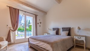 A bedroom with a large bed, a nightstand, a chair, and a view of the outdoors through a sliding door. - Macs Reve - A dream for bikers : 2 bikes for men & 2 bikes for women available for free. (Collobrières)