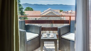 A balcony with wicker furniture, a small table with cups and a teapot, and a view of the sea and mountains.