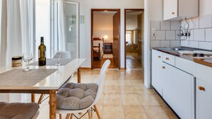 A modern kitchen with white cabinets, a dining area with a table and chairs, and a visible hallway leading to a bedroom.