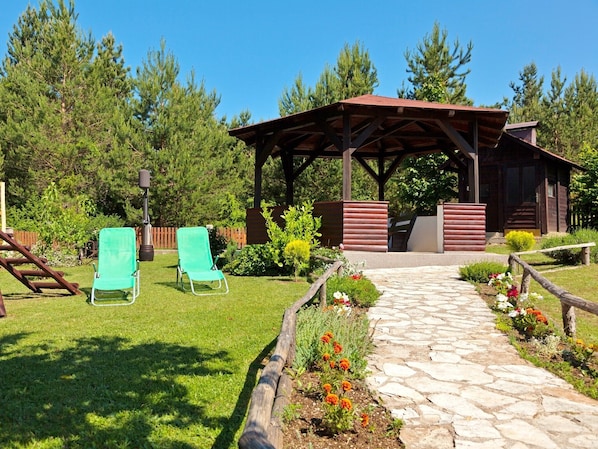 A gazebo, two lawn chairs, a stone pathway, and a wooden fence in a garden setting.
