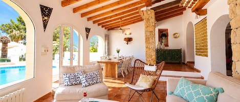 A spacious living area with a pool view, wooden beams, stone pillar, and a dining area.