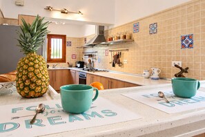Een keuken met houten kastjes, een ananas op het aanrecht en twee teal mokken op tafelonderzetters.