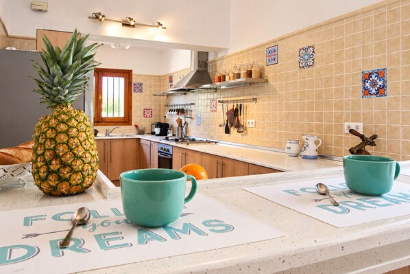 A kitchen with wooden cabinets, a pineapple on the counter, and two teal mugs on placemats.