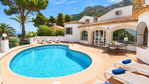 Une piscine privée, dotée de chaises longues et d’un espace repas, le tout entouré d’arbres et avec une chaîne de montagnes en toile de fond.