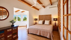 Une chambre à coucher avec un grand lit, une tête de lit en bois, deux tables de chevet avec des lampes, une commode avec des tiroirs et un ventilateur de plafond.