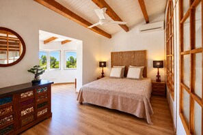 Un dormitorio con una cama grande, cabecera de madera, dos mesitas de noche con lámparas, un aparador con cajones y un ventilador de techo.
