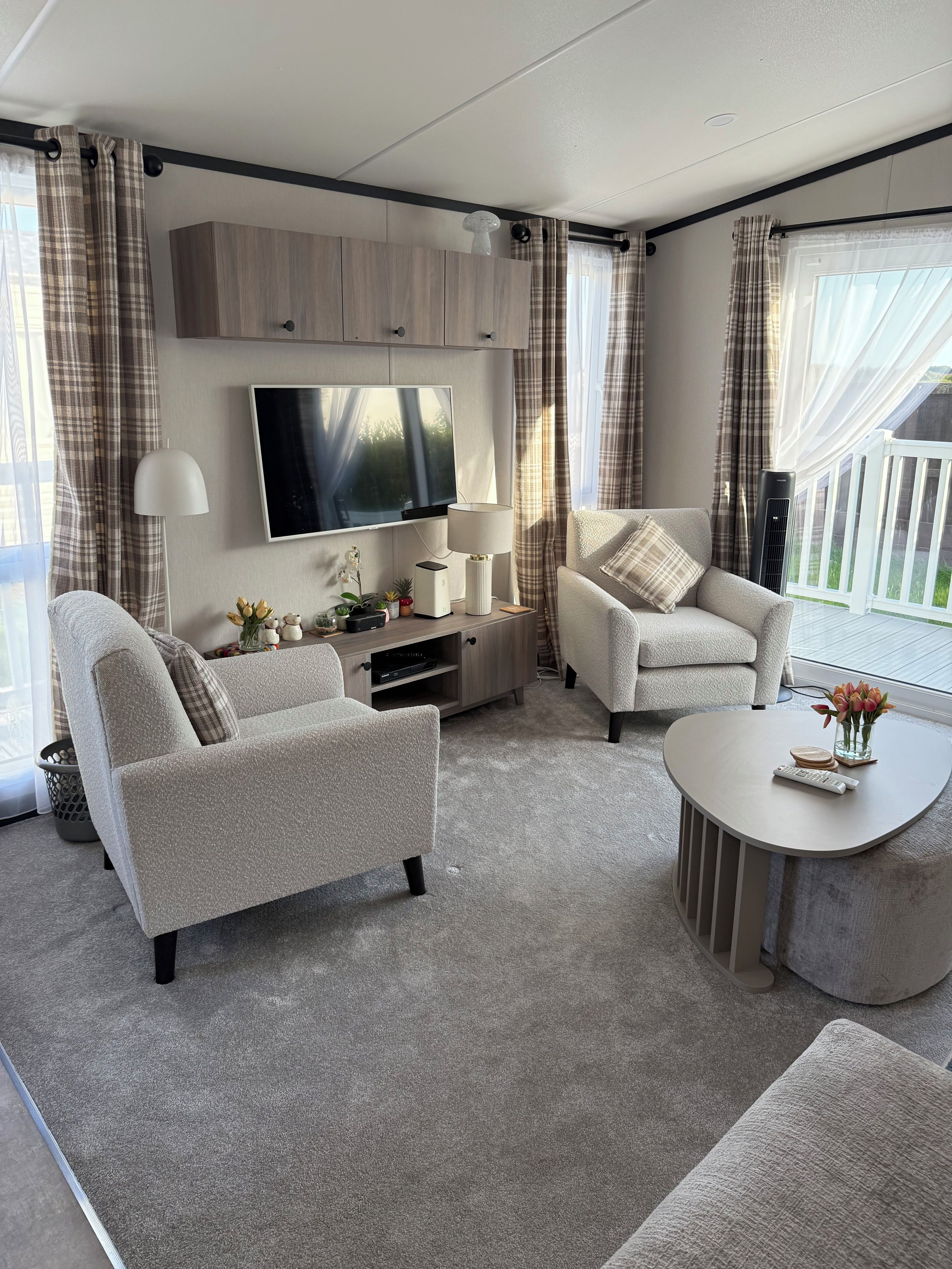 A modern living room with a flat-screen TV, two armchairs, a coffee table, and a TV stand with decorative items.