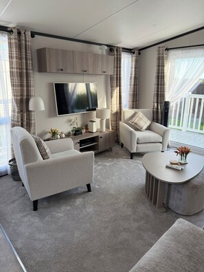 A modern living room with a flat-screen TV, two armchairs, a coffee table, and a TV stand with decorative items.