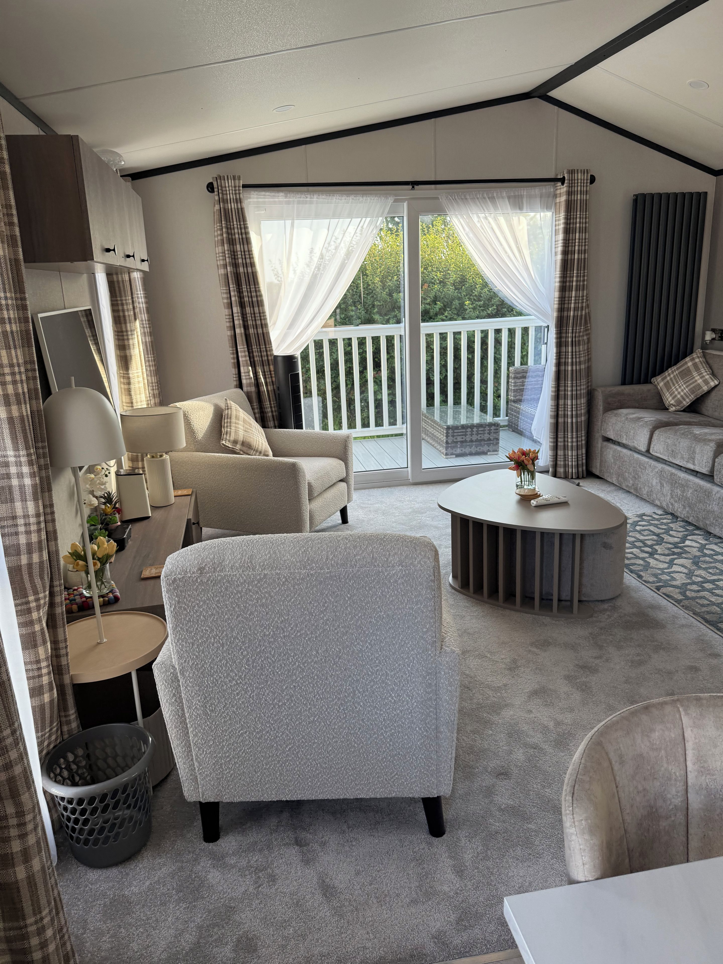 Ein modernes Wohnzimmer mit Sofa, Sessel und Couchtisch, ein Balkon mit Geländer und ein großes Fenster mit Vorhängen.