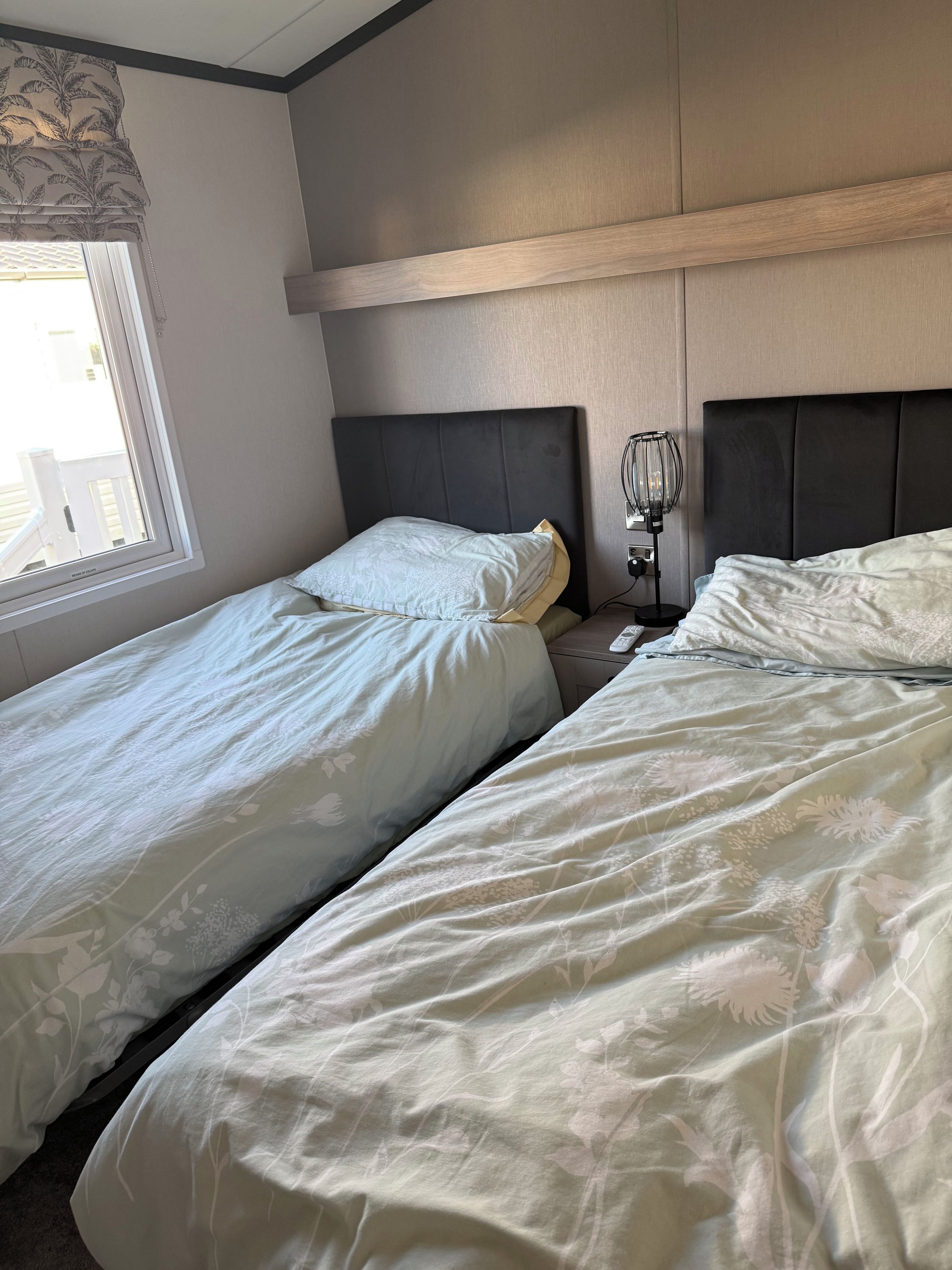 A hotel room with two beds, a bedside table, a lamp, and a window with a view.