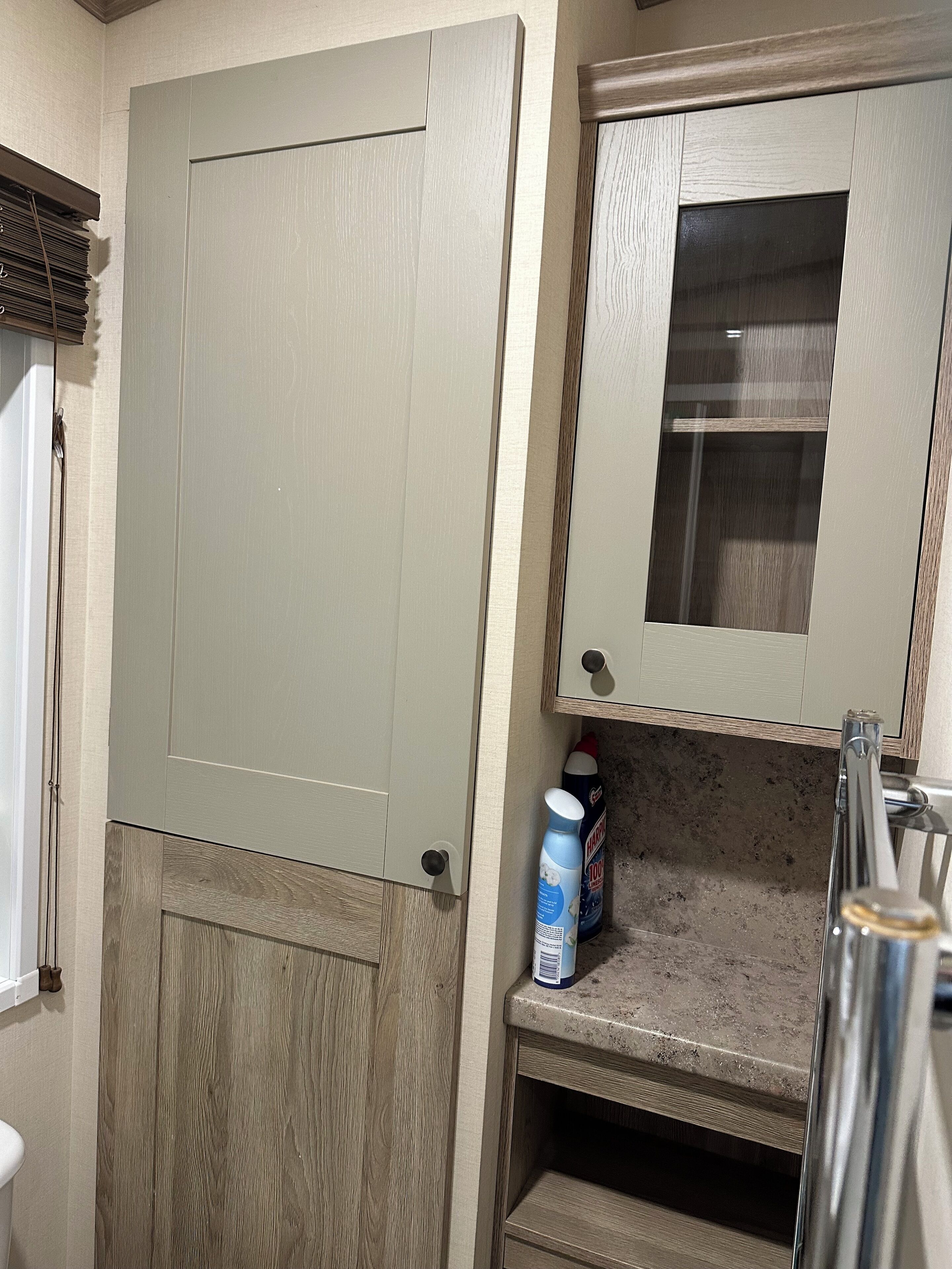 Un baño con puerta de madera, un armario espejo y una encimera con productos de limpieza.