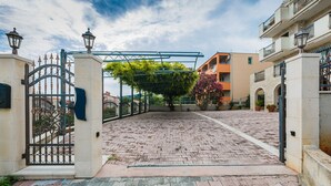 Un patio amurallado con un sendero empedrado, un pérgola con vegetación y edificios con balcones.