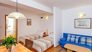 Una habitació acollidora amb dos llits, una taula de menjador amb un vas de flors, un sofà blau i una taula de fusta petita.