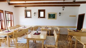 Un comedor con mesas y bancos de madera, techo de madera con vigas a la vista y faroles fijados a la pared.