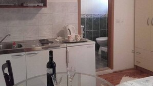 Une cuisine compacte équipée d’un évier, d’une bouilloire, d’un petit réfrigérateur, d’une table à manger avec une bouteille et des verres, et donnant sur la salle de bain adjacente.