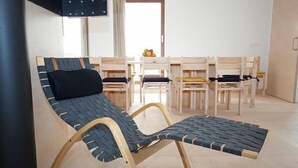 A room with a single reclining chair with a woven seat and backrest, a wooden table with chairs, and a flat-screen TV mounted on the wall.