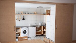 A compact kitchen with a washing machine, wooden cabinets, and a dining area with a table and chairs.