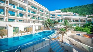 A hotel with a large swimming pool, multiple balconies, and a view of a green hillside. - Monte Casa Spa And Wellness (Petrovac)
