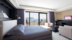 A hotel room with a bed, a TV, a sofa, a desk, and a balcony with a view of the sea. - Monte Casa Spa And Wellness (Petrovac)