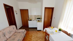 A compact living space with a sofa, dining table, chairs, a kitchen area, and wooden doors. - Apartments Anđelko, (11891), Diklo, hr (Diklo)