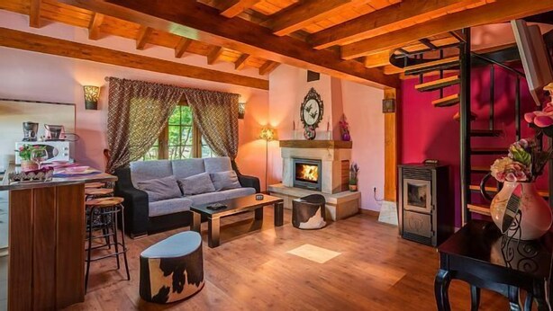 A cozy living room with a fireplace, wooden beams, a sofa, and a dining area.