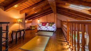 A cozy loft bedroom with wooden beams, a sofa bed, a desk, and a view of the outdoors.