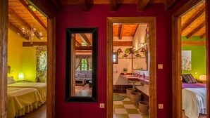 A room with wooden beams, a checkered floor, a mirror, and a bed with a yellow bedspread.