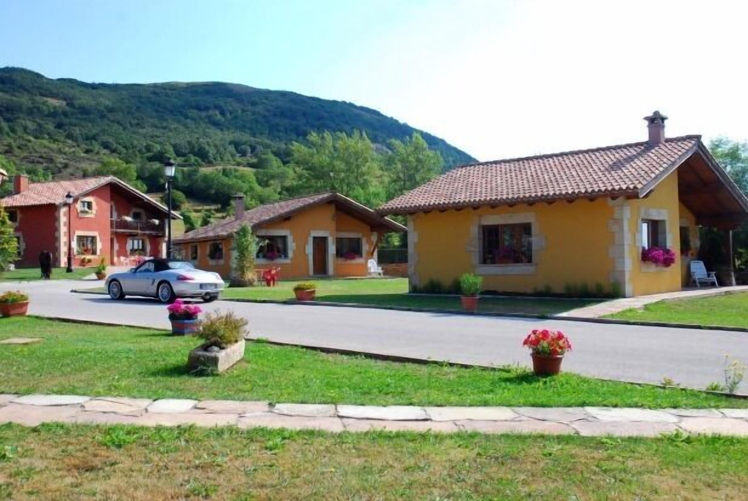 A row of yellow houses with red roofs, a white car parked in front, and a mountain in the background.