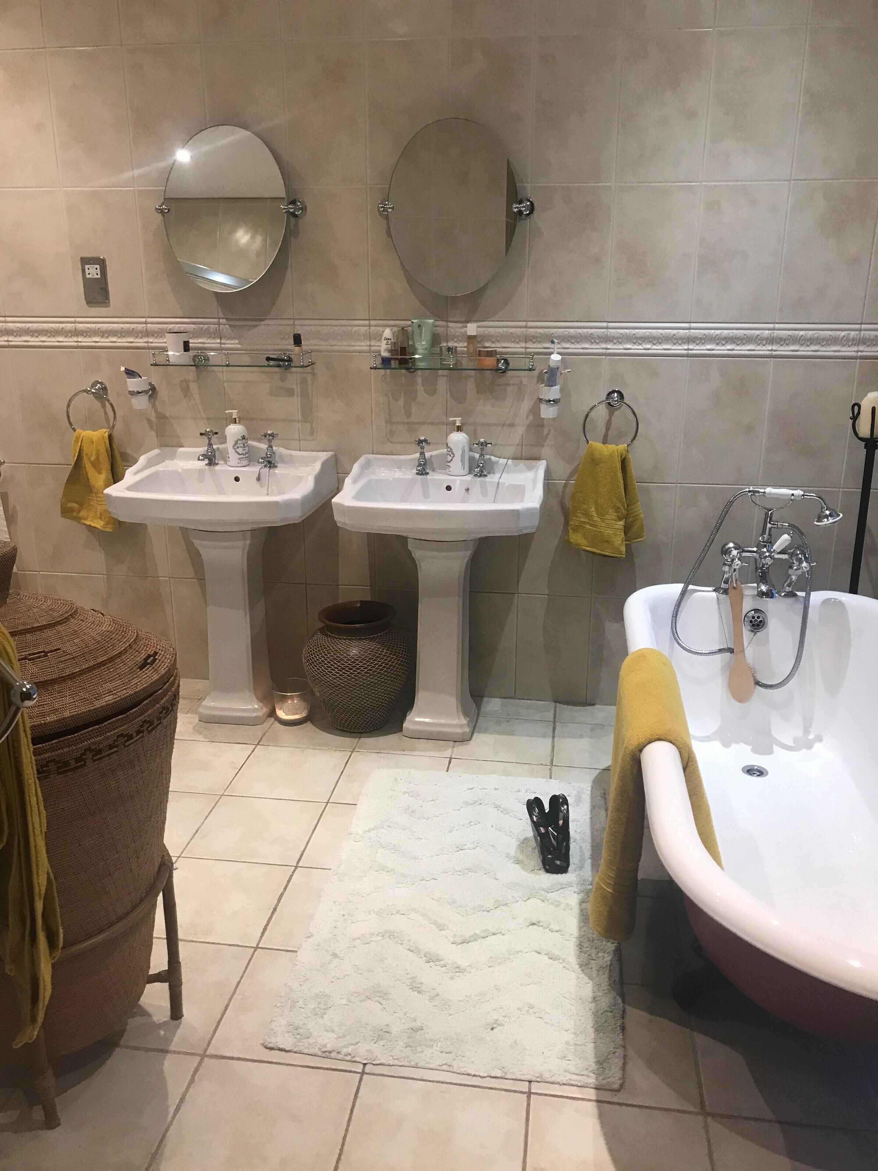 Ein Badezimmer mit zwei Waschbecken, einer Badewanne und einem Spiegel über jedem Waschbecken. Handtücher hängen an Haken und ein kleiner Teppich liegt auf dem Boden.