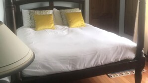 A four-poster bed with white bedding and two yellow pillows, a wooden floor, and a small table with a lamp. - Idyllic and Unique House on the Lake  (Whitegate)