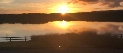 Un coucher de soleil sur un lac paisible, avec une clôture en bois au premier plan.