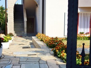 Stroll through the beautifully landscaped entrance, lined with vibrant potted plants and leading to a modern building with a striking archway.