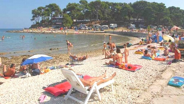 A beach with people sunbathing, swimming, and walking along the shore. - Apartments Snježana, (15028), Medulin, hr (Medulin)