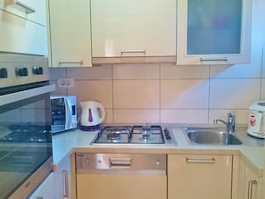 Compact kitchen with oven, microwave, and gas stove, featuring a stainless steel sink and ample storage.