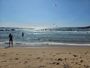 Ein Strand mit Fußspuren im Sand, ein klarer Himmel und Menschen im Wasser.