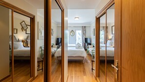 Hotellihuone, jossa on suuri peili, puulattia, kaksi sänkyä, yöpöydät, lamput ja ikkuna, jossa on verhot.