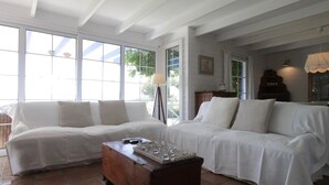 A spacious living room with two white sofas, a wooden coffee table, and a large window providing natural light.