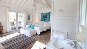 A bedroom with two beds, a large window, a ceiling fan, and a bathroom with a bathtub and sink.