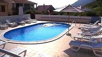 Relax by the clear pool surrounded by a deck with lounge chairs and a shaded area.