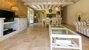 Un salón amplio con televisor, mobiliario blanco y una pared de piedra.