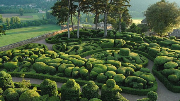Un jardín cuidadosamente diseñado con patrones geométricos de setos y un sendero de piedra.