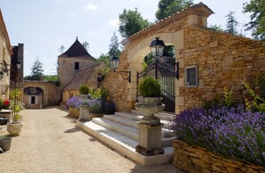 A stone building with a tiled roof, a small tower, and steps leading to a gate.