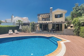 Uma piscina com espreguiçadeiras, um alpendre coberto e um edifício de dois andares com varanda.