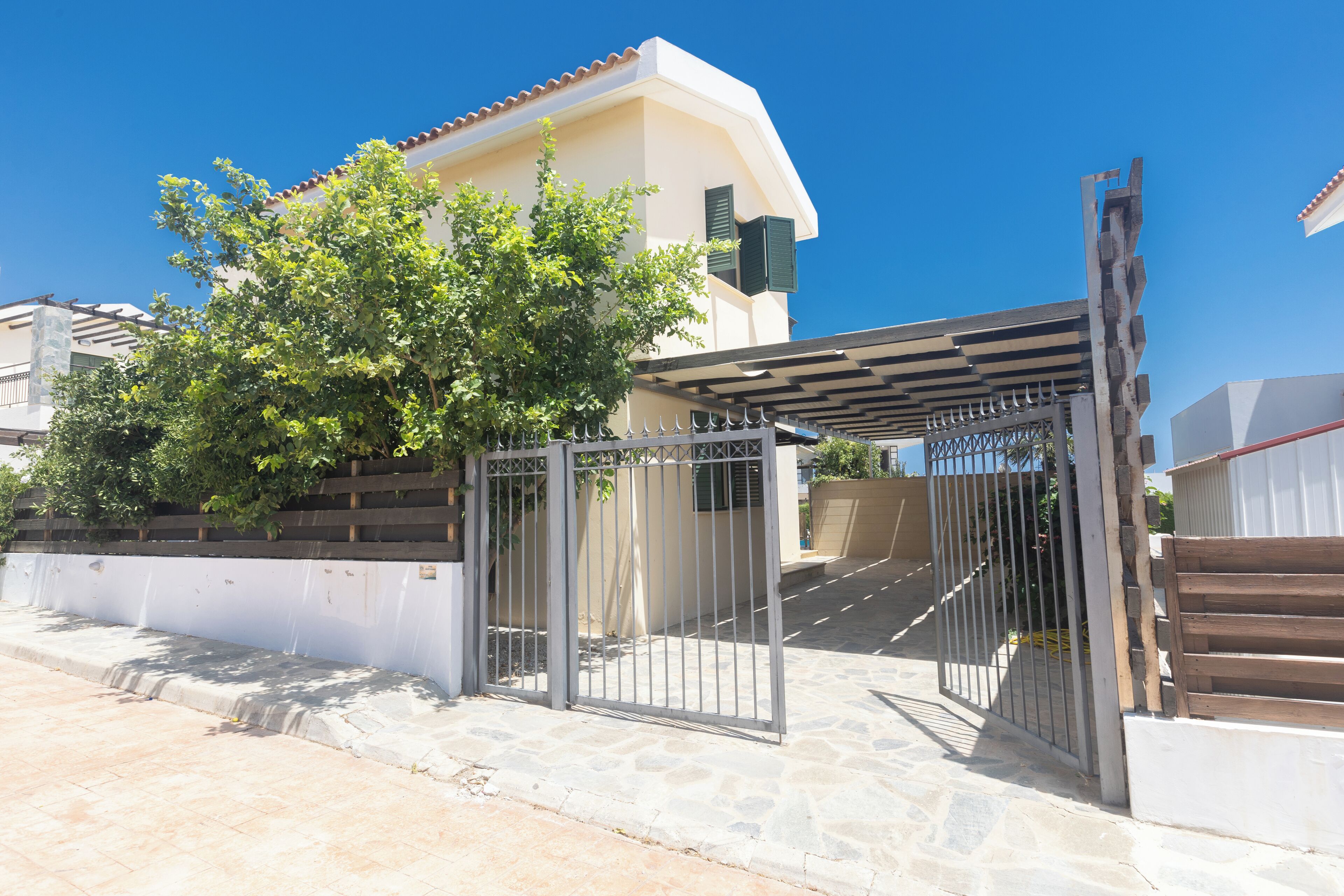 A gated entrance to a building with a stone pathway leading to a covered area with a pergola.