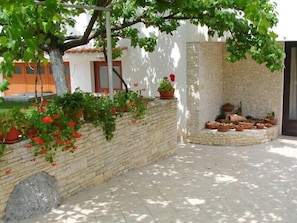 Relax in a serene outdoor space surrounded by lush greenery and vibrant flowers, with a shaded stone bench and a beautiful view.